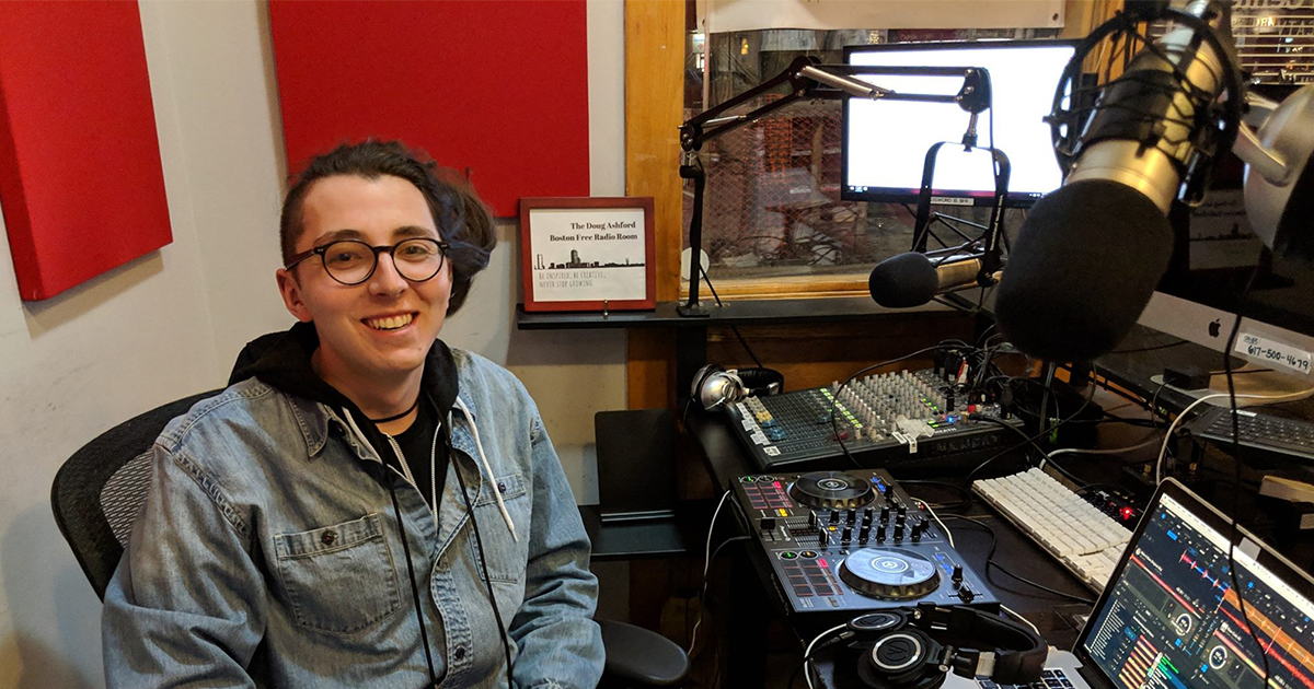 Producer sits in audio production studio in front of microphones, laptop and mixer